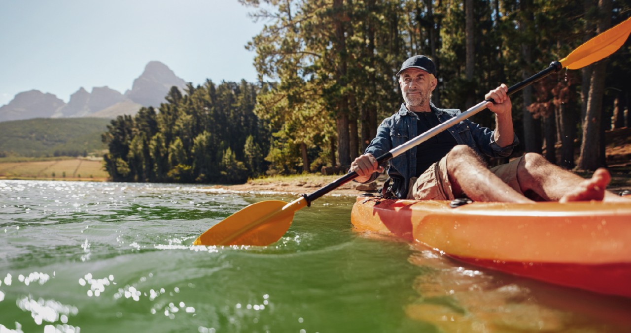 Senior man paddles orange kayak down river