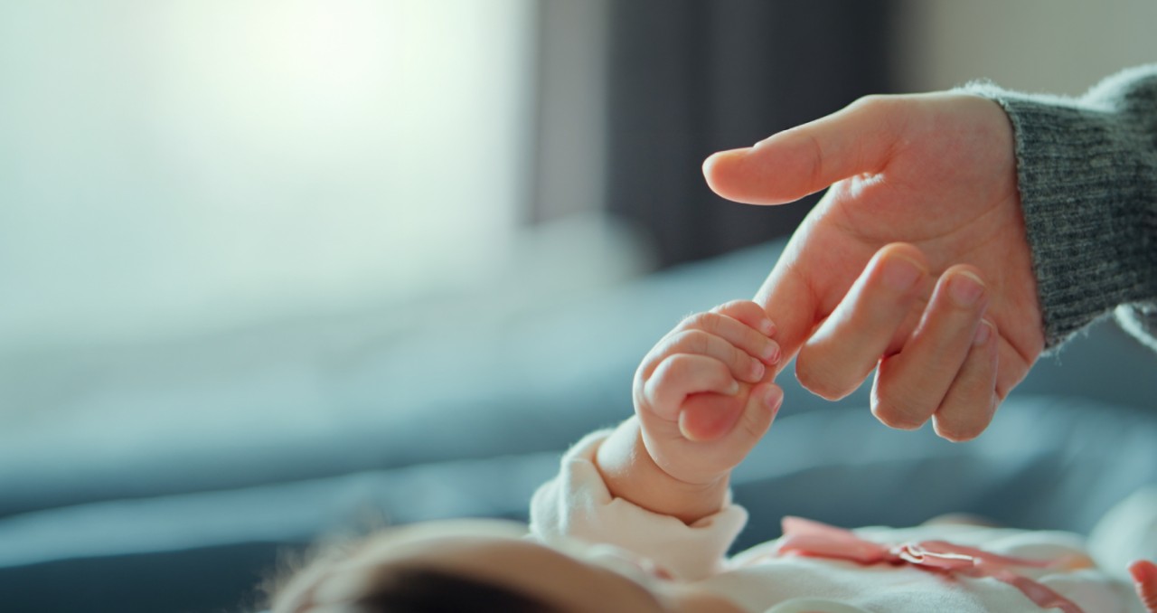 An infant reaches up and grips an adult finger