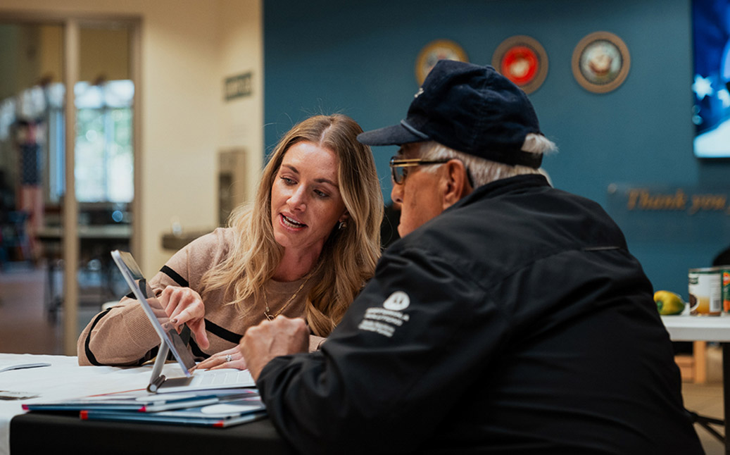 An outreach specialist shows a senior veteran some information on a tablet