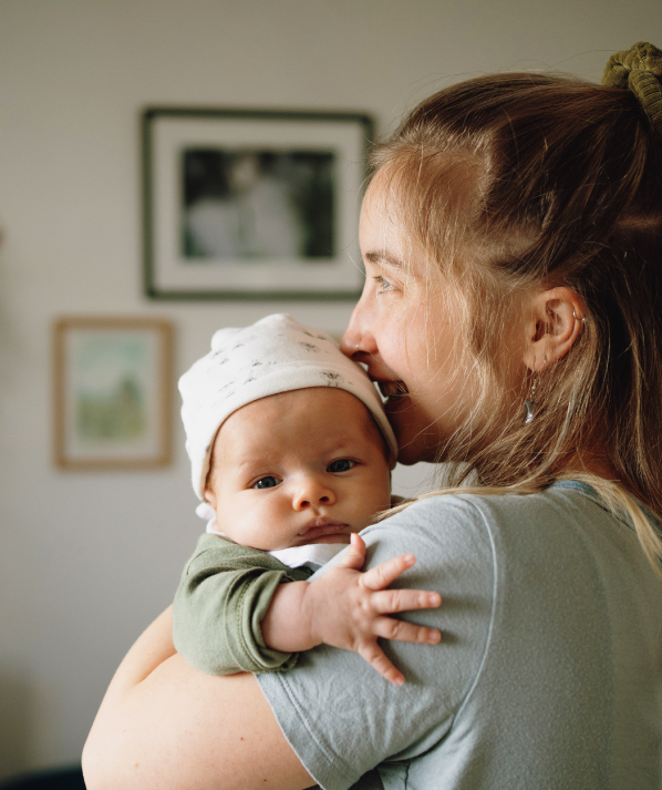 A young mother holds an infant who is looking into camera