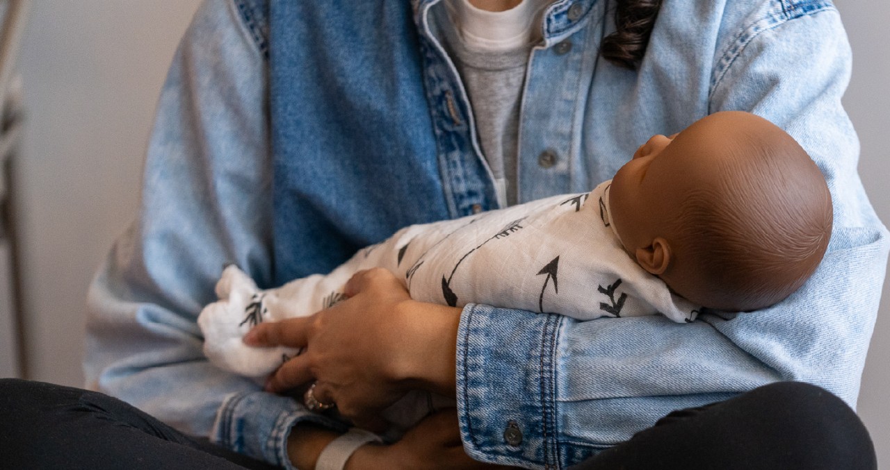 Young woman holding a swaddled infant doll