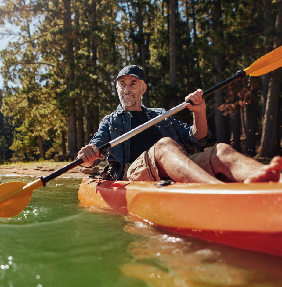 Senior man paddles orange kayak down river