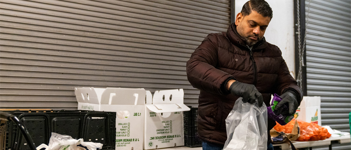 A man wearing a coat and gloves puts food in a bag