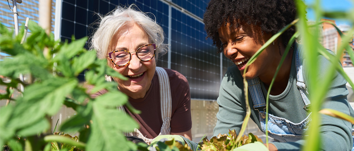 older woman with white hair laughs in garden with younger african american woman
