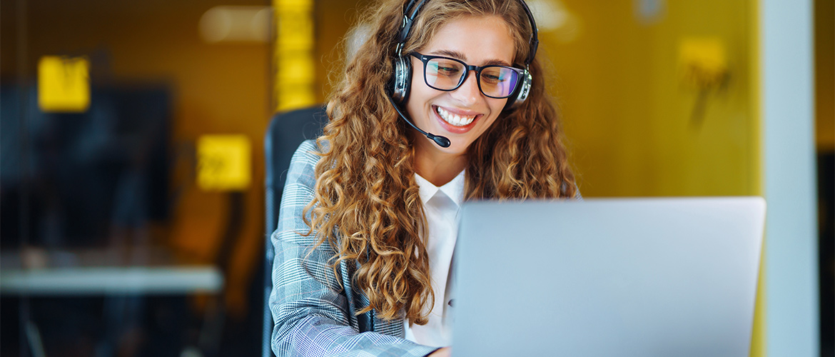 A woman speaks using a telehone headset while typing on a laptop