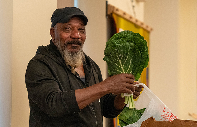 An older man holds up collard greens from a box of produce