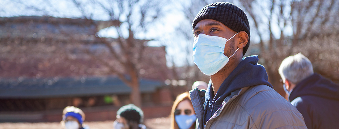 Black man in COVID mask stares off among masked group