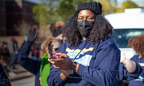 Black woman in COVID mask claps during street parade