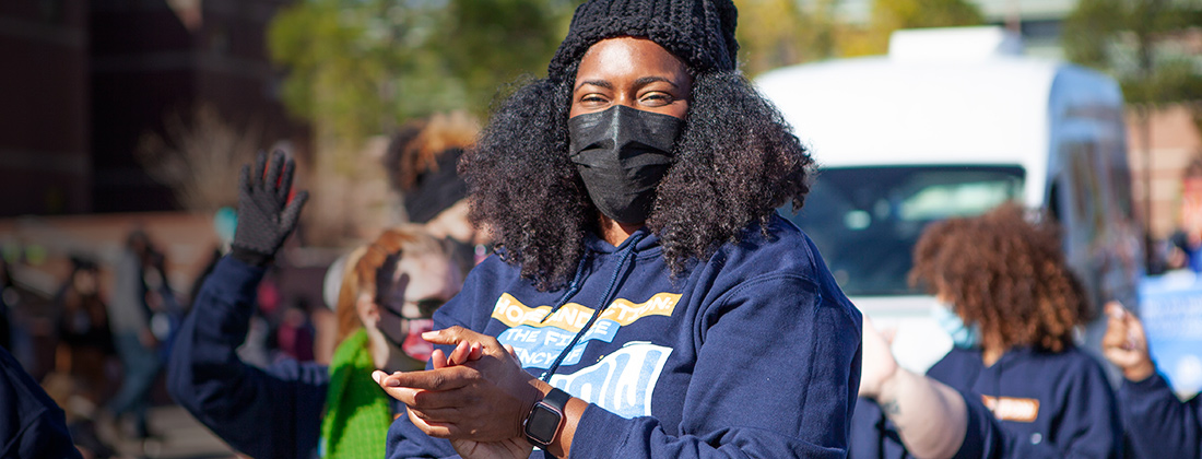 Black woman in COVID mask claps during street parade