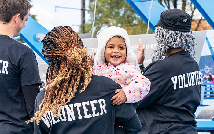 Volunteer holds smiling young girl at fitness park