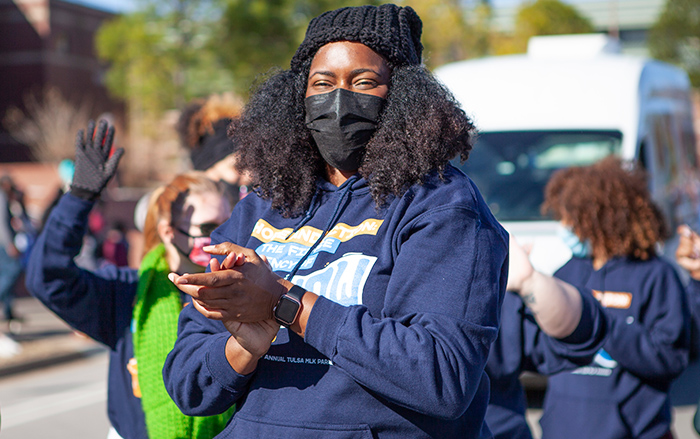 Black woman in COVID mask claps during street parade