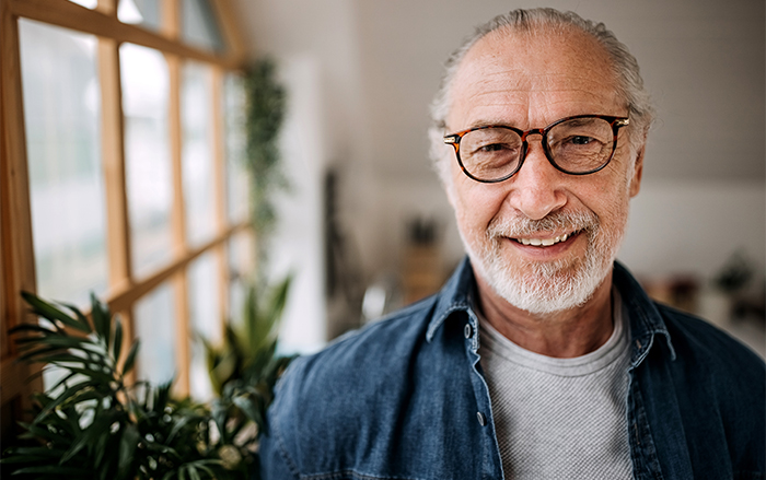 Man in glasses smiles near plants bordering a window