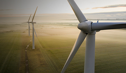 Wind turbines generate energy in haze-filled field.