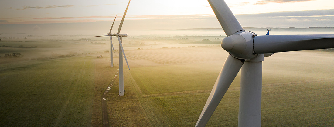 Wind turbines generate energy in haze-filled field.