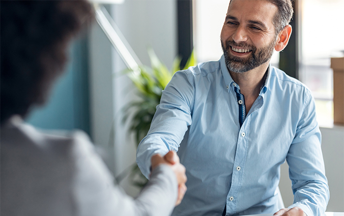 White bearded man in blue work shirt smiles while shaking hands